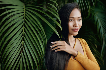 Hair beauty. Woman model with long straight hair in palm leaves