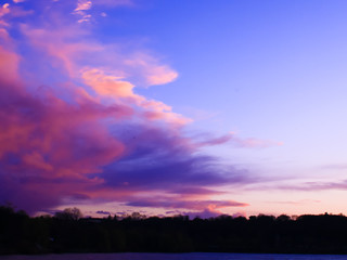Fototapeta premium Big pink cloud coming over trees and lake in the countryside. Clouds threatening rose at sunset