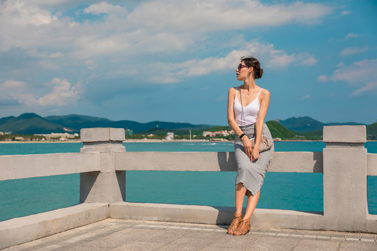 Cheerful and beautiful girl resting fun in vacation, on the pier on background of city. In China, Hainan city of Sanya. View of island in bay. Town Sanya is popular tourist destination in China