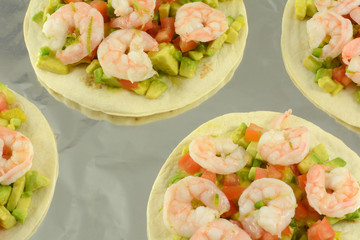 Shrimp tostados with chopped avocado and tomatoes on aluminum foil lined baking sheet