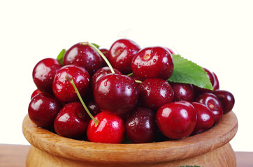 Sweet cherry fruits with leaves in a wooden bowl on a white background