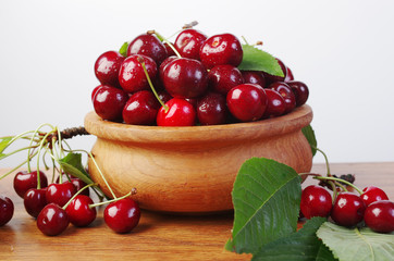 Sweet cherry fruits with leaves in a wooden bowl on a white background