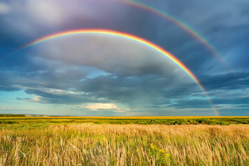 Rainbow over stormy sky. Rural landscape with rainbow over dark stormy sky in a countryside at...