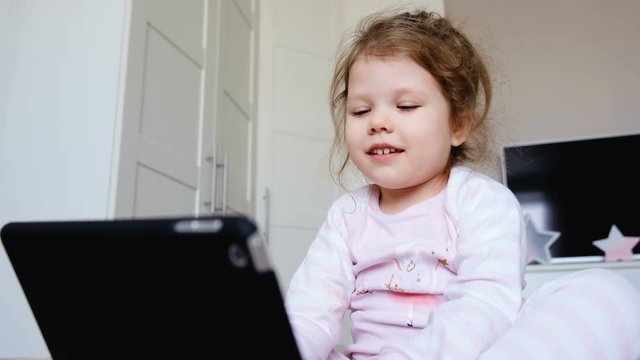 Funny little girl watching a cartoon on the tablet and repeating the movement for her favorite characters. Concept of educational activities for young children