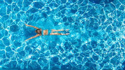 Active girl in swimming pool aerial drone view from above, young woman swims in blue water,...