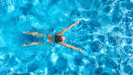Active girl in swimming pool aerial drone view from above, young woman swims in blue water,...