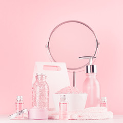 Spa cosmetics products and round mirror in pastel pink and silver color - cream, bath salt, essential oil, soap, bottle, bowl, towel on white wood shelf.