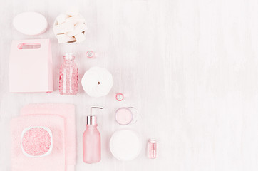 Spring fresh cosmetic products for makeup and bath in pastel pink color on white wooden board as decorative border, top view.