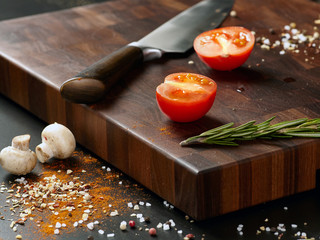 Closeup of a beautiful dark cutting board with a knife and a sliced tomato