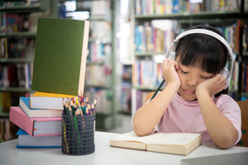Cute asian little girl reading a book and headphones listening to music,
