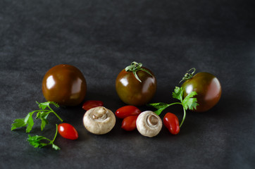 Black and red tomatoes, white button mushrooms and parsley on a dark background