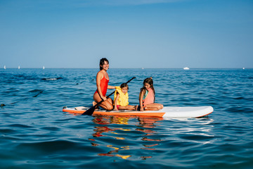 Mother with two daughters stand up on a paddle board