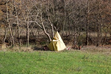 A yellow tipi style tent made of canvas at a river bank under deciduous trees at autumn in front of...