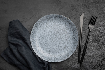 Stylish table setting with black cutlery. Empty plate, table textile and black cutlery on black...