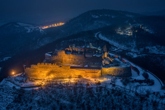 Visegrad, Hungary - Aerial view of the beautiful, illuminated high castle of Visegrad at blue hour with snowy hills of Pilis on a winter night