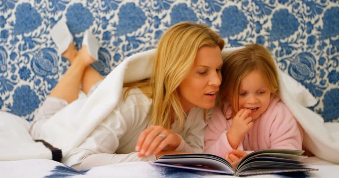 Front view of young Caucasian mother and daughter looking at photo album on bed at home 4k