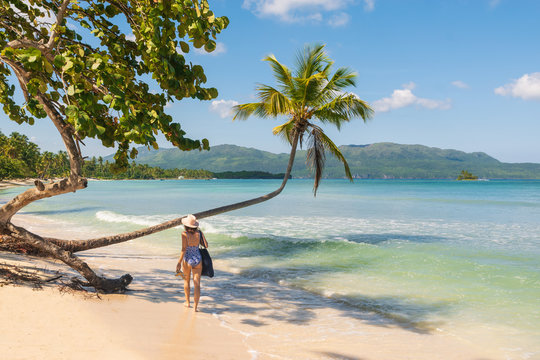 Attractive girl in bikini and hat walk on beach under the palm tree in Las Galeras.