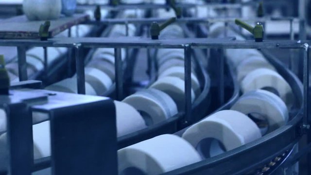 Closeup of conveyor and paper tissue rolls moving on it. Selective focus. Industrial background. Pulp and paper industry concept.	Motion blur. Blue