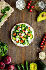 Cooking fresh salad. Vegetables, greens, spices, plate of salad on dark wooden kitchen desk top view
