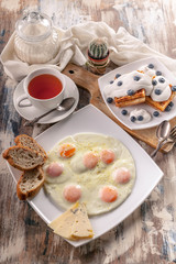 Fried eggs, Viennese waffles, tea on a wooden background. Vertical shot