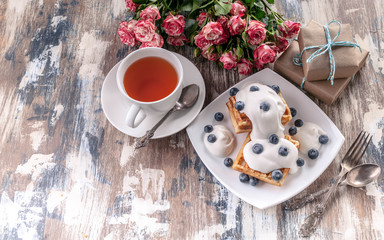 Women's day concept. Belgian waffles with blueberries, gift boxes and roses, a cup of tea.