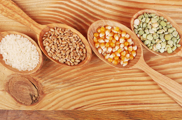 Seeds of peas, corn, wheat, beans, rice in wooden spoons on a wooden table