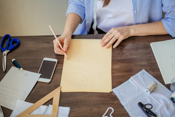 Unrecognizable woman drawing sketch on blank craft paper sheet sitting on desktop with sketches, close up