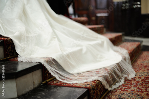 Cola de vestido de novia blanco sobre alfombra roja con estampado en escalera de altar