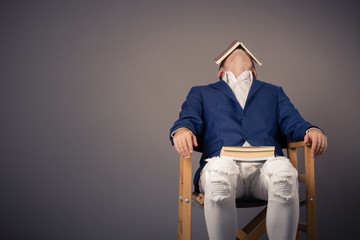 Tired of reading! Man sitting in chair with book on head, feeling bored after studying and taking a...
