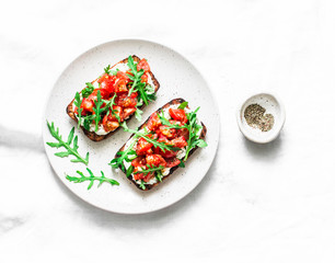 Tomatoes and arugula salad whole grain bread sandwiches on a light background, top view. Copy space