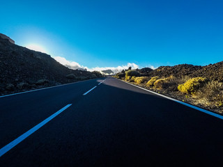 Long way road at the mountain with vulcan mount in front and blue clear sky - ground point of view with black asphalt and white lines - driving and travel concept