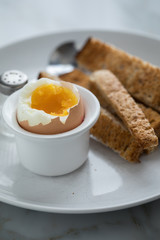 Gekochtes Ei im Eierbecher mit Eierlöffel, Salzstreuer und Toast Brot beim Frühstück