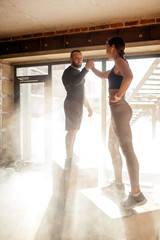 Fototapeta na wymiar Young athletic woman thanking his personal fitness coach, giving encouraging him high five standing on plyo boxes, surrounded by dust particles