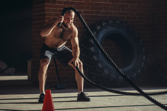 Sport concept. Caucasian athlet with naked torso with rope in functional training at outdoor gym in a crossfit workout over brick wall background.