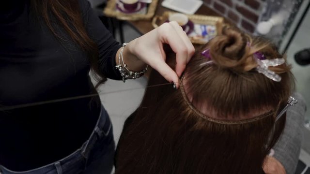 The hairdresser sews artificial hair to the real thing. The process of hair extension. 4K
