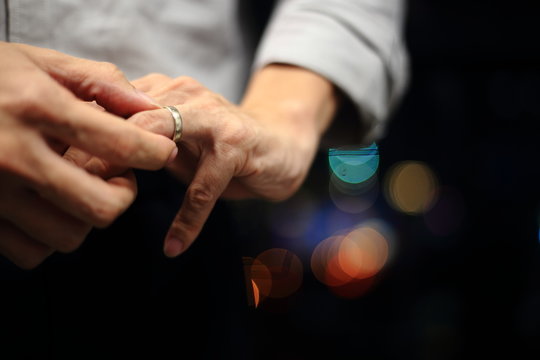 Man Putting On Wedding Ring. Close Up Shot Of Man Fidgeting Ring With Nice Out Of Focus Urban Light Backgrounds.