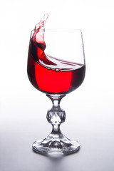 Red wine splashing in wine glass on light background. .