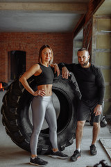 Young and beautiful sports couple standing beside big tire while training in the gym