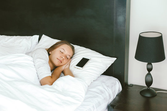 Girl sleeping in bed with smartphone beside