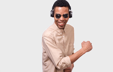 African American young man with headphones listen the music and dancing. Happy smiling Afro male wearing mirror sunglasses and casual outfit, posing over white studio background. People concept