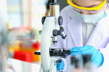 Young woman scientist wearing safety glass,mask and gloves was using microscope in laboratory.