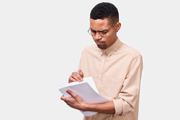 Confident African American man entrepreneur in beige shirt, writing financial report checking incomes with blank copy space for advertising. Pensive male executive analyzing documentation. Business