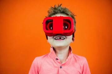 funny boy plays in glasses of virtual reality for the phone on a bright orange background