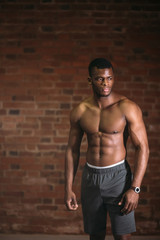 Fototapeta na wymiar Strong afroamerican athletic man with naked perfect shape muscular body looking at camera isolated over brick background.