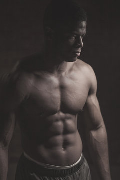 Toned image of strong afroamerican athletic man with naked perfect shape musculs standing isolated over dark background.