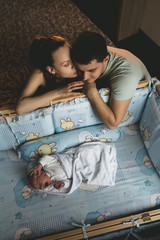 Man and a woman near their newborn. Parents kiss. Boy cries in his crib. Mom, dad and baby. Portrait of young family. Family life. Man was born.