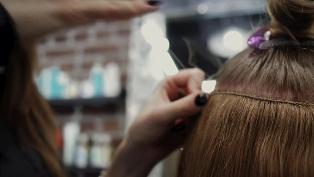 The hairdresser sews artificial hair to the real thing. The process of hair extension. 4K