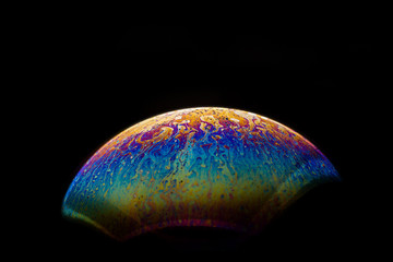 A bubble in rainbow colors on a black background.