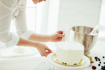 talented experienced woman scraping the excess icing off the cake. close up side view photo.