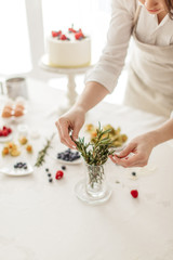 woman in apron choosing leaves for decoration of cake, close up cropped photo.
